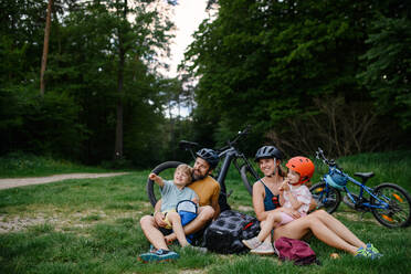 Eine junge Familie mit kleinen Kindern ruht sich nach einer Radtour im Sommer im Gras eines Parks aus. - HPIF01986