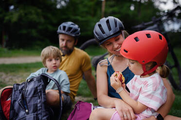 Eine junge Familie mit kleinen Kindern ruht sich nach einer Radtour im Sommer im Gras eines Parks aus. - HPIF01988