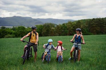 Ein Porträt einer jungen Familie mit kleinen Kindern, die sich auf eine Fahrradtour vorbereiten, stehend mit Fahrrädern in der Natur. - HPIF01989