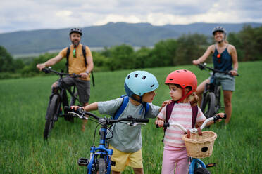 Ein Porträt einer jungen Familie mit kleinen Kindern, die sich auf eine Fahrradtour vorbereiten, stehend mit Fahrrädern in der Natur. - HPIF01990