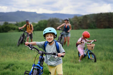 Ein Porträt einer jungen Familie mit kleinen Kindern, die sich auf eine Fahrradtour vorbereiten, stehend mit Fahrrädern in der Natur. - HPIF01991