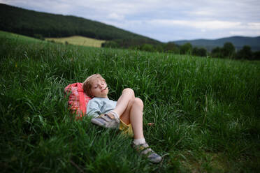 Ein glücklicher erster Schultag: Ein müder Schuljunge mit Rucksack liegt im Gras. - HPIF01994