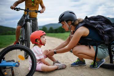 A mother and father helping their little daughter after falling off bicycle outdoors - HPIF01996