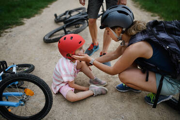 A mother and father helping their little daughter after falling off bicycle outdoors - HPIF01997