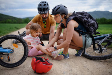 Eine Mutter und ein Vater helfen ihrer kleinen Tochter nach einem Sturz vom Fahrrad im Freien - HPIF01998