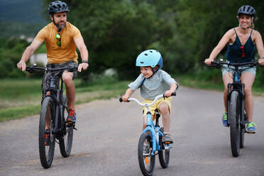 A young family with little child riding bicycles on road in village in summer. - HPIF02004