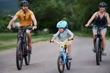 Eine junge Familie mit kleinem Kind fährt im Sommer mit dem Fahrrad auf der Straße in einem Dorf. - HPIF02004