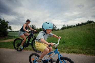 Eine junge Familie mit kleinem Kind fährt im Sommer mit dem Fahrrad auf der Straße in einem Dorf. - HPIF02006