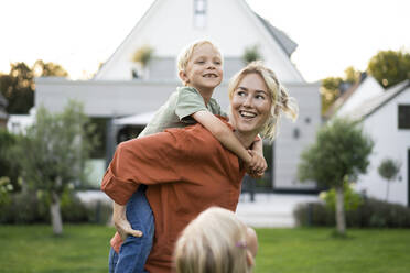 Happy mother giving piggyback ride to daughter in back yard - JOSEF15028