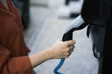Hand einer Frau, die den Stecker eines Ladegeräts für Elektroautos hält - JOSEF15034