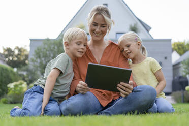Lächelnde Mutter zeigt Kindern im Hinterhof einen Tablet-PC - JOSEF15042
