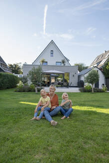 Lächelnde Frau mit Kindern im Gras sitzend im Hinterhof - JOSEF15048