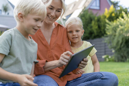 Smiling woman using tablet PC by children in garden - JOSEF15049