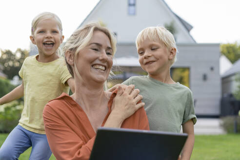 Glückliche Mutter hält Tablet-PC genießen mit Kindern vor dem Haus - JOSEF15054