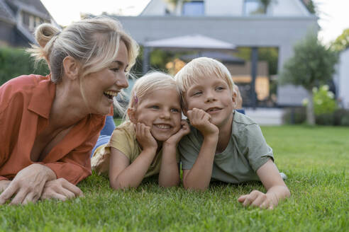 Glückliche Mutter betrachtet ihre Kinder, die sich im Garten auf die Ellbogen stützen - JOSEF15060