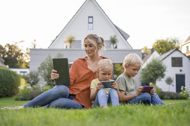 Family with wireless technologies sitting on grass in garden - JOSEF15068