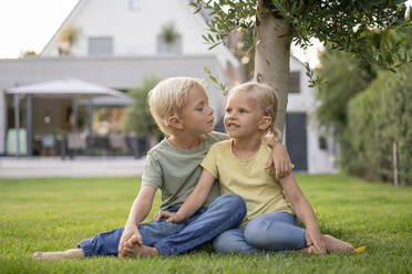 Junge mit blonden Haaren sitzt mit Arm um Schwester auf Gras im Hinterhof - JOSEF15071