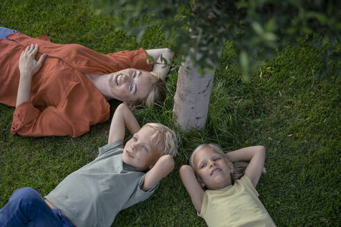 Lächelnde Mutter mit Kindern, die sich im Hinterhof im Gras ausruhen - JOSEF15080