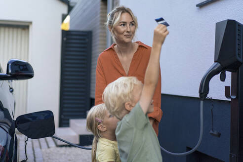 Junge zahlt vor Schwester und Mutter mit Kreditkarte für Ladegerät für Elektrofahrzeuge - JOSEF15087