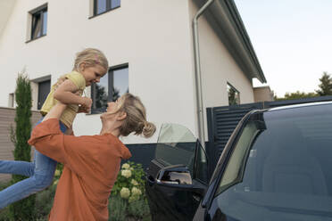 Happy mother carrying daughter by car in front of house - JOSEF15103