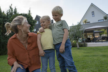 Happy woman looking at children in back yard - JOSEF15119