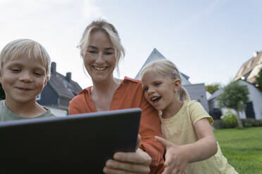 Glückliche Frau teilt Tablet-PC mit Kindern im Hinterhof - JOSEF15123