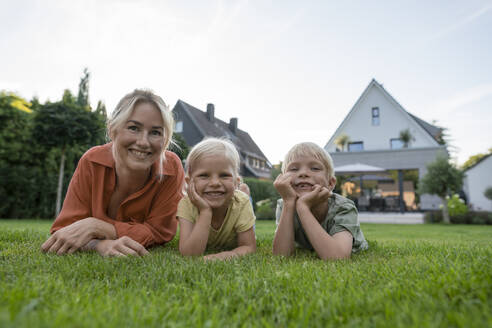 Lächelnde Frau mit Kindern, die sich im Hinterhof auf die Ellbogen stützen - JOSEF15125