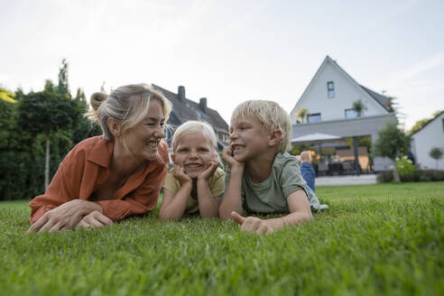 Happy woman with children leaning on elbows in back yard - JOSEF15126