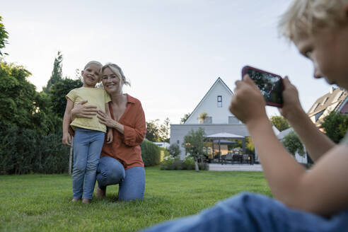 Junge fotografiert Mutter und Schwester mit dem Smartphone im Garten - JOSEF15132