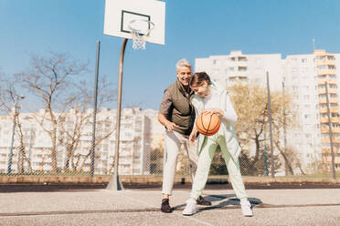 Ein glücklicher Vater und seine Teenager-Tochter spielen draußen auf dem Platz Basketball. - HPIF02013