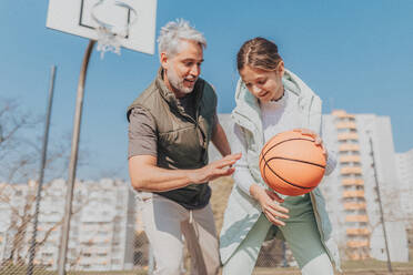 Ein glücklicher Vater und seine Teenager-Tochter spielen draußen auf dem Platz Basketball. - HPIF02014