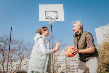 Ein glücklicher Vater und seine Teenager-Tochter spielen draußen auf dem Platz Basketball. - HPIF02016