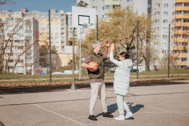 Ein glücklicher Vater und seine Teenager-Tochter spielen draußen auf dem Platz Basketball und geben sich die Hand. - HPIF02018