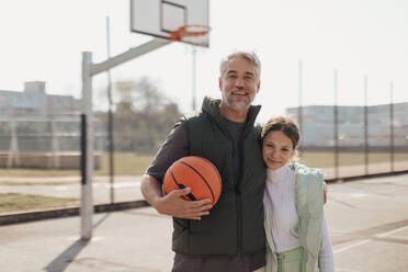 A happy father and teen daughter embracing and looking at camera outside at basketball court. - HPIF02021