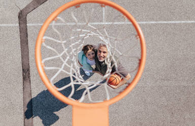A happy father and teen daughter embracing and standing under a basketball hoop net, directly above - HPIF02022