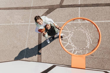 Vater und Tochter im Teenageralter spielen draußen auf dem Platz Basketball, Blick von oben auf das Netz des Basketballkorbs. - HPIF02025