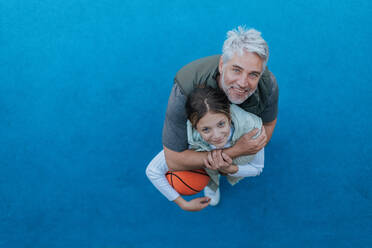 Ein Vater und eine Tochter im Teenageralter spielen draußen auf dem Platz Basketball, hoher Blickwinkel. - HPIF02027