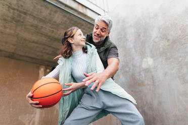 Ein glücklicher Vater und seine Teenager-Tochter spielen draußen auf dem Platz Basketball. - HPIF02031