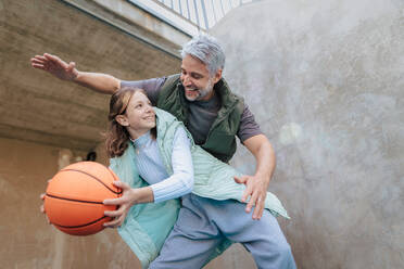 Ein glücklicher Vater und seine Teenager-Tochter spielen draußen auf dem Platz Basketball. - HPIF02032