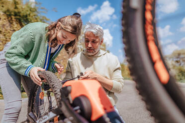 Ein glücklicher Vater mit seiner Tochter im Teenageralter repariert ein Fahrrad auf der Straße in der Stadt. - HPIF02034