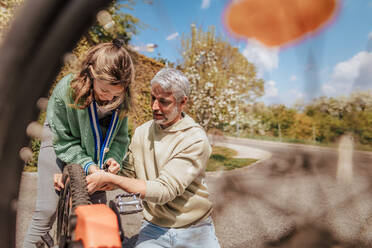 Ein glücklicher Vater mit seiner Tochter im Teenageralter repariert ein Fahrrad auf der Straße in der Stadt. - HPIF02035