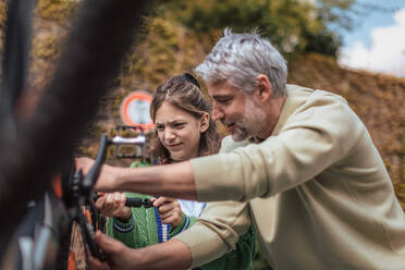 A happy father with teenage daughter repairing bicycle in street in town. - HPIF02037