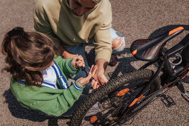 A happy father with teenage daughter repairing bicycle in street, high angle view. - HPIF02038