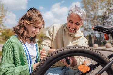 Ein glücklicher Vater mit seiner Tochter im Teenageralter repariert ein Fahrrad auf der Straße in der Stadt. - HPIF02039