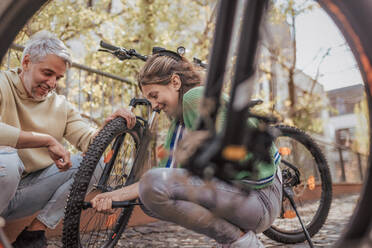 A happy father with teenage daughter repairing bicycle in street in town. - HPIF02040