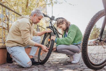 Ein glücklicher Vater mit seiner Tochter im Teenageralter repariert ein Fahrrad auf der Straße in der Stadt. - HPIF02041