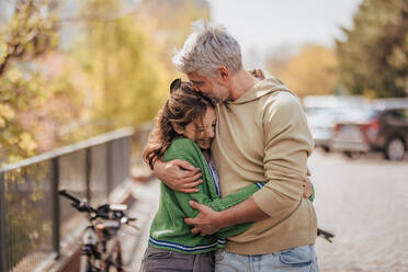 Eine Tochter im Teenageralter umarmt ihren Vater draußen in der Stadt, wenn sie Zeit miteinander verbringen. - HPIF02044