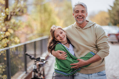 Eine Tochter im Teenageralter umarmt ihren Vater draußen in der Stadt, wenn sie Zeit miteinander verbringen. - HPIF02045