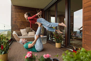 Ein glücklicher Vater und seine Teenager-Tochter machen gemeinsam akrobatische Übungen auf dem Balkon. - HPIF02070