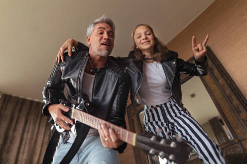 A father rock guitarist having fun and and dancing with his teenage daughter at home. - HPIF02077